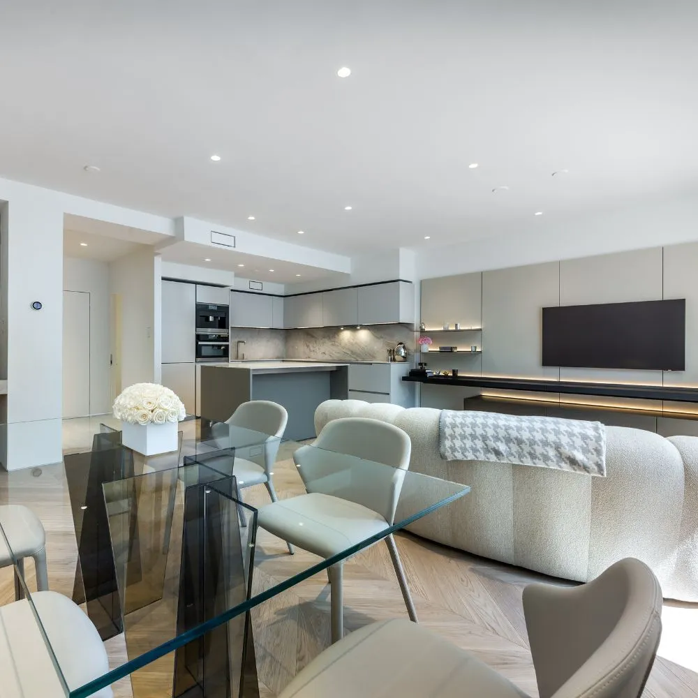 Open-concept living area with a glass dining table, cream chairs, and a gray sofa in a sleek modern kitchen.