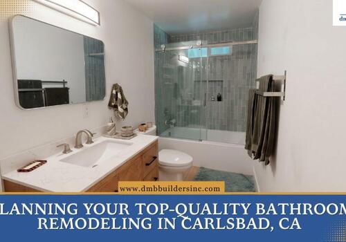 A vertical photograph of a modern bathroom with light wood cabinetry, a white countertop and sink, a pill-shaped mirror, and a linear light fixture.