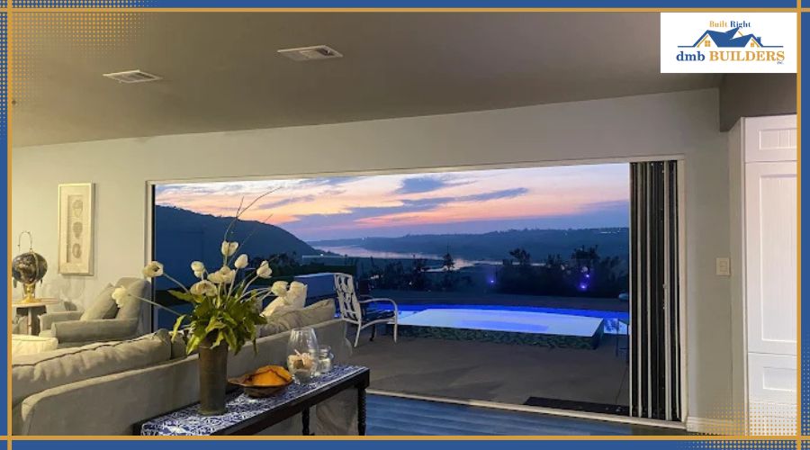 Expert Full Home Remodeling in Rancho Santa Fe CA Luxury living room with large glass folding doors opening to a backyard pool and scenic sunset view, featuring the dmb Builders logo.